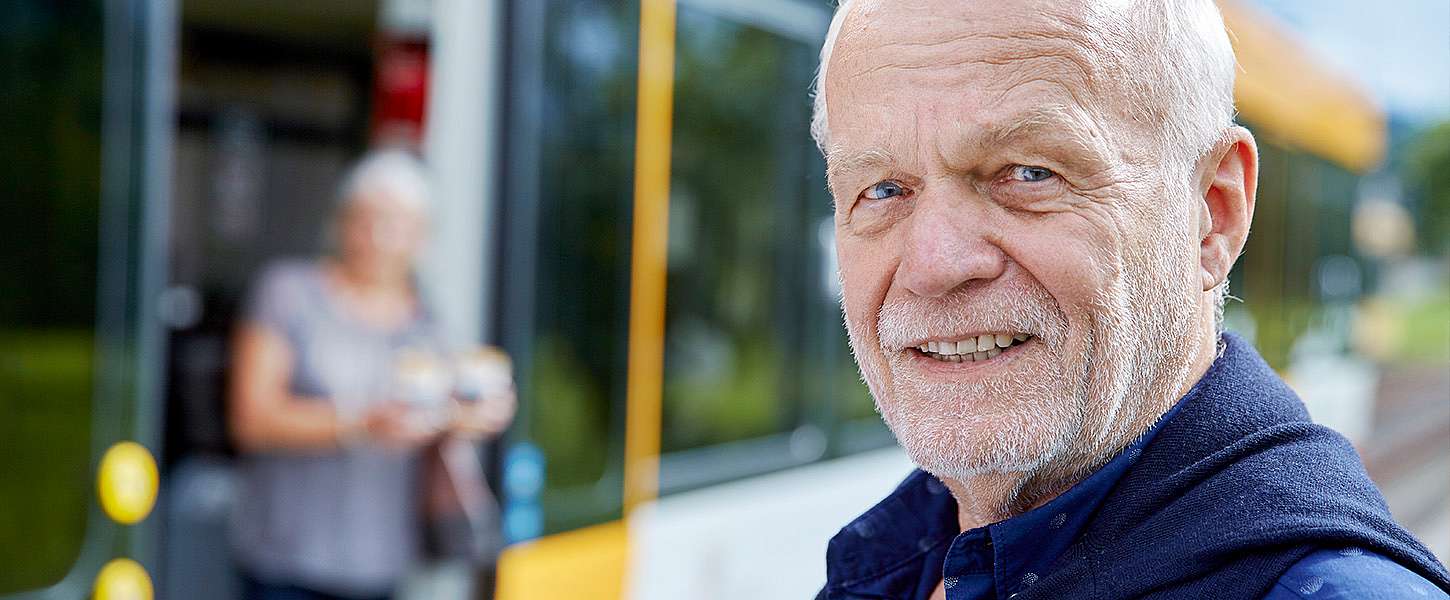 Ein älterer Mann steht an einer Bahnhaltestelle. Verschwommen im Hintergrudn erkennt man eine Frau beim aussteigen aus der Bahn.