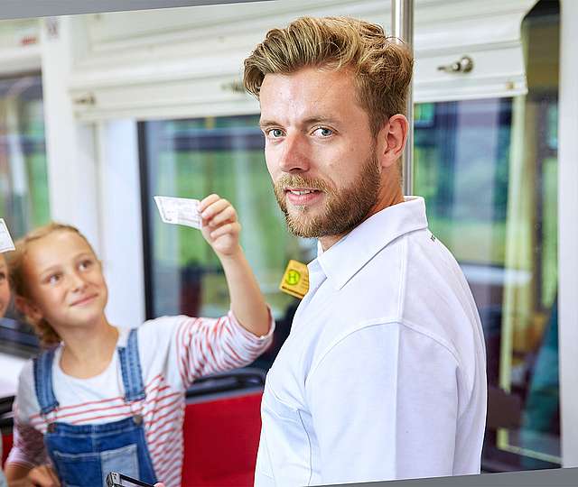 Zwei Mädchen zeigen einem Fahrscheinprüfer ihre Fahrkarten.