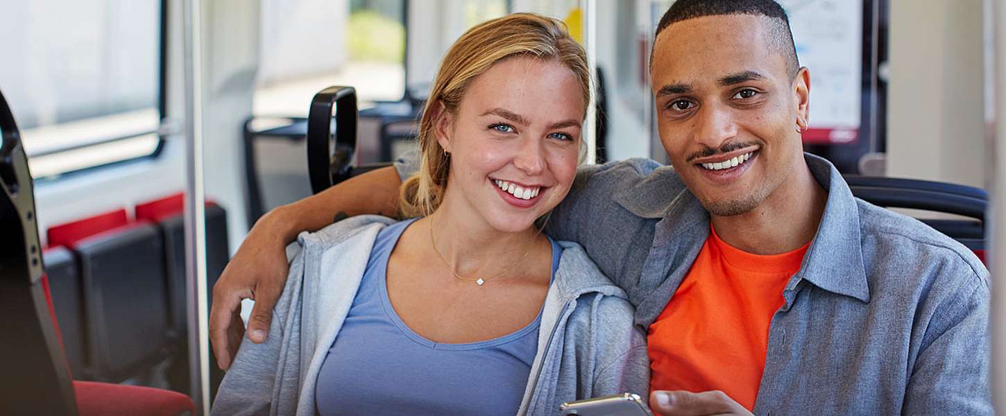 Ein junges Pärchen sitzt in der Bahn mit einem Smartphone in der Hand.