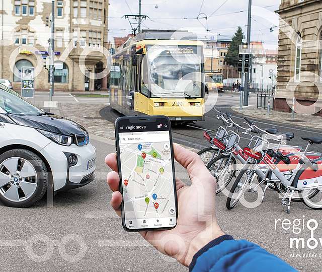 Hand mit Smartphone. Im Hintergrund Auto, Fahrräder und Bahn zu sehen.