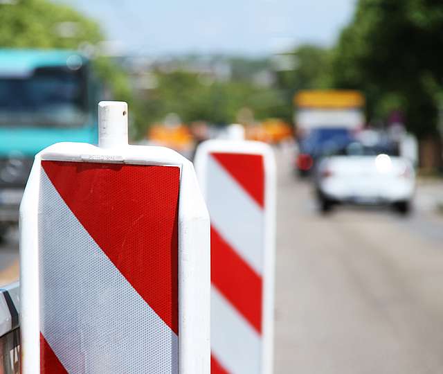 Eine Verkehrsabsperrung an einer Straße. Verschwommen im Hintergrund sieht man ein Auto und einen LKW