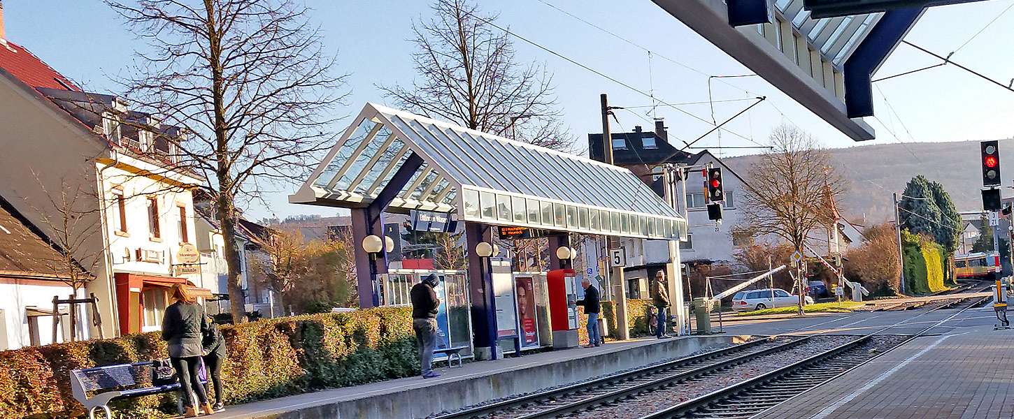 An einer überdachten Haltestelle warten Fahrgäste auf die einfahrende Straßenbahn.