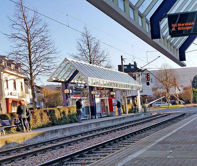 An einer überdachten Haltestelle warten Fahrgäste auf die einfahrende Straßenbahn.