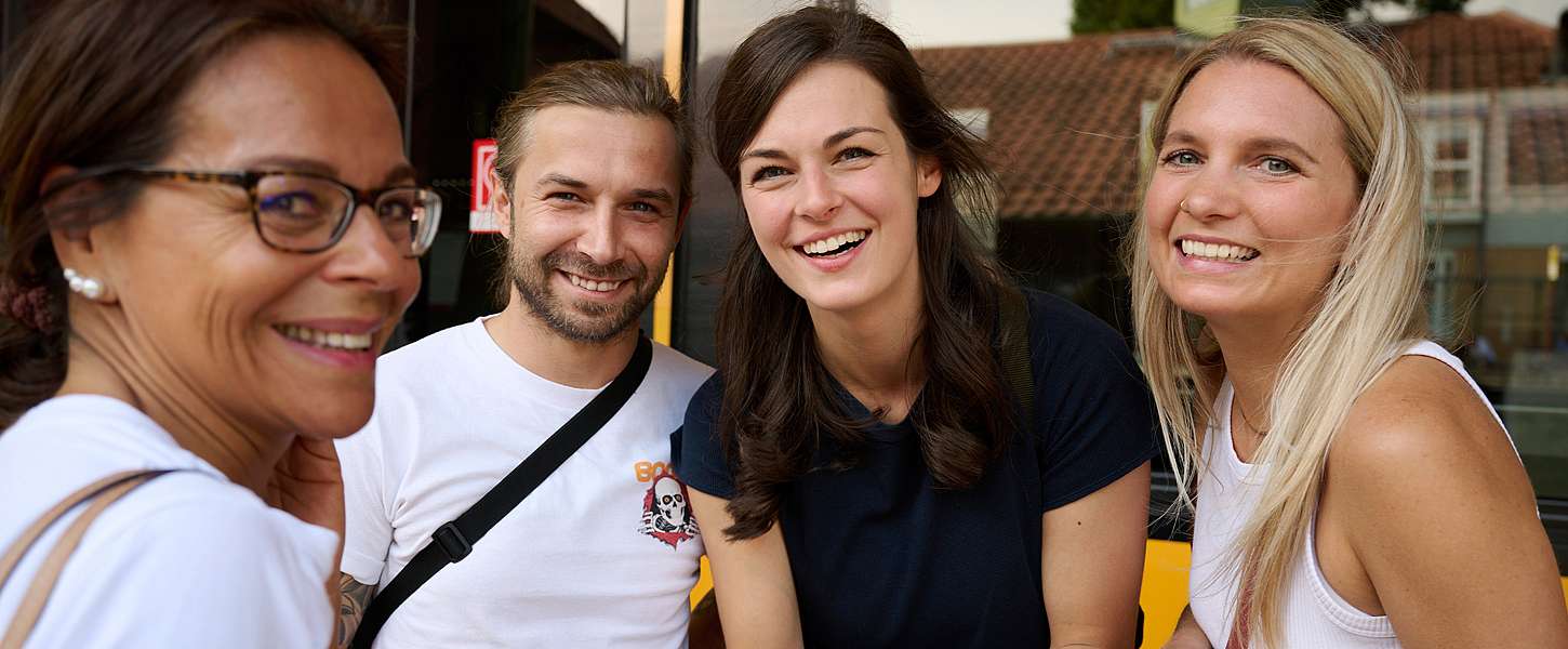 4 junge Menschen stehen lächelnd zusammen.