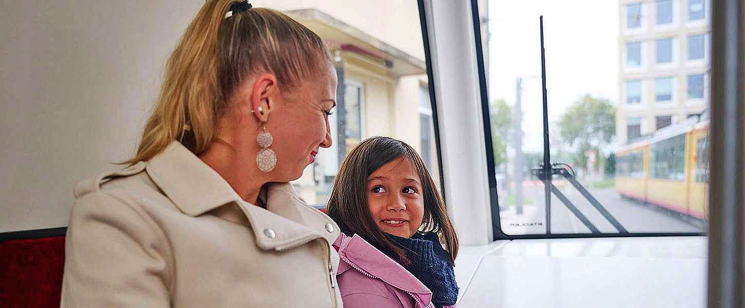 Eine Mutter und ihre Tochter sitzen in einer Bahn und lächeln sich an.