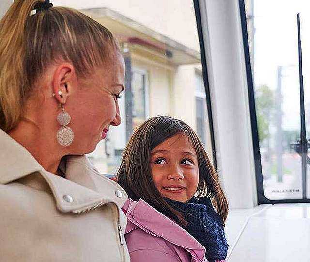 Eine Mutter und ihre Tochter sitzen in einer Bahn und lächeln sich an.