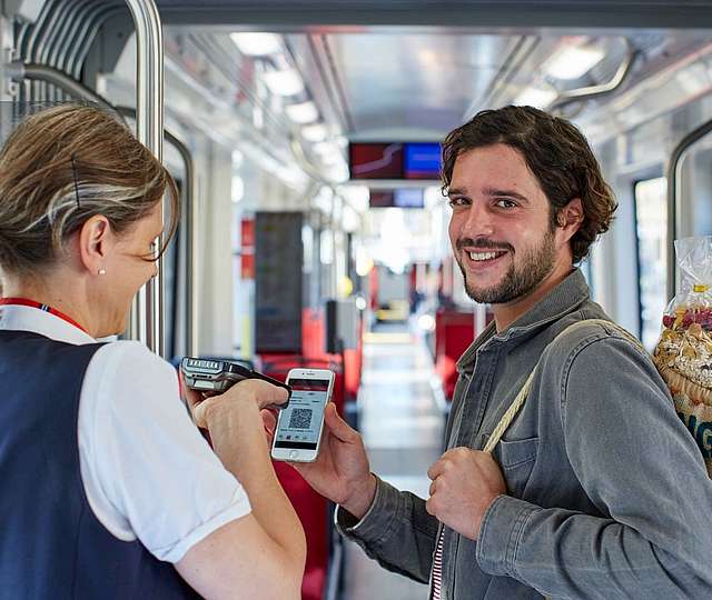 Mann zeigt einer Kontrolleurin seine Fahrkarte auf dem Smartphone.