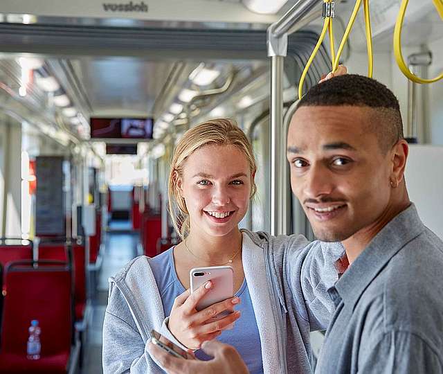 Eine junge Frau und ein junger Mann stehen mit Handy in der Bahn.