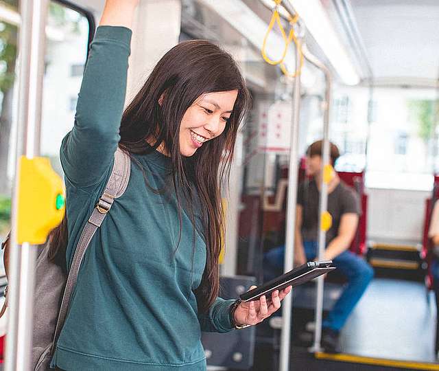 Eine Frau steht lächelnd in einer Bahn. Sie schaut auf ein Tablet in ihrer Hand.