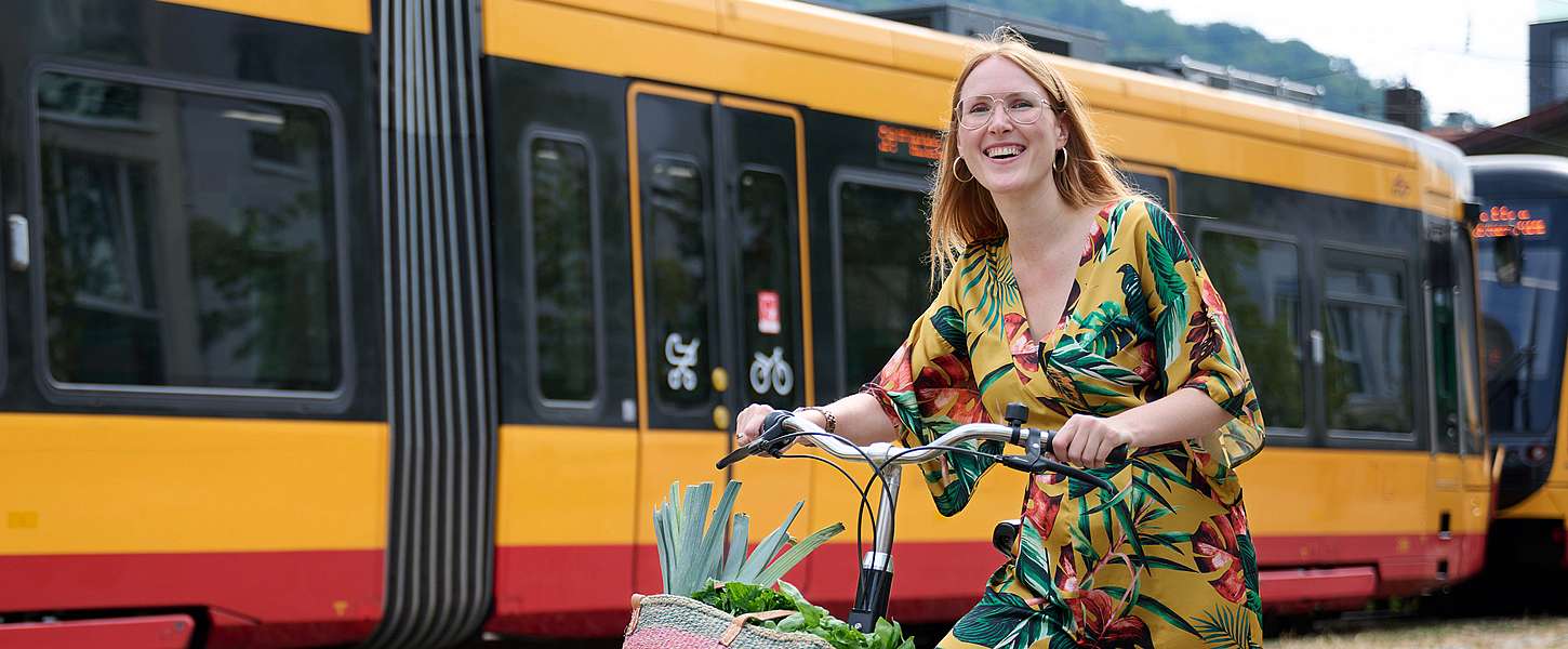 Eine junge Frau fährt mit einem KVV.nextbike an einer KVV-Bahn vorbei.