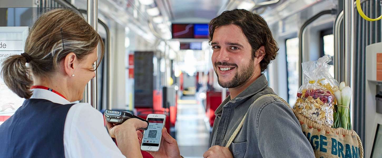 Mann zeigt einer Kontrolleurin seine Fahrkarte auf dem Smartphone.