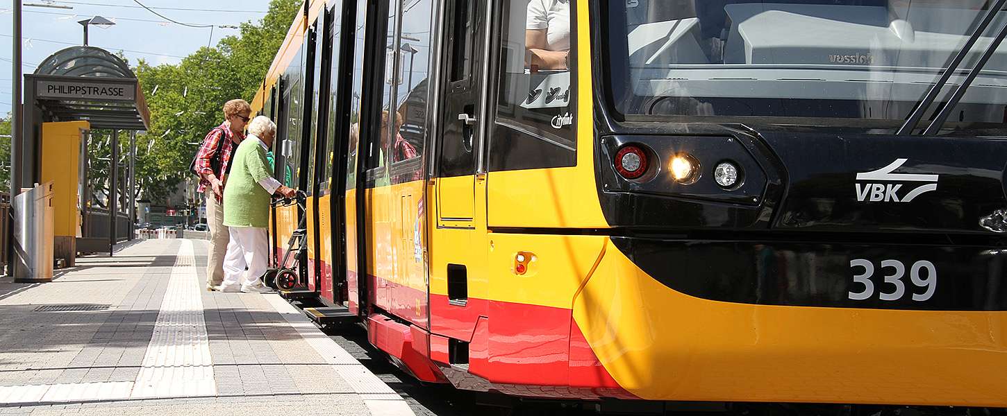 Zwei Frauen steigen in eine Niederflurbahn ein. Eine der Frauen hat einen Rollator.