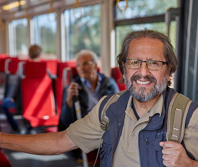 Ein älterer Mann mit Rucksack steht in der Bahn.