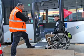 Ein Mitarbeiter der Verkehrsbetriebe Karlsruhe gibt einem Fahrgast, der in einem Rollstuhl sitzt, Tipps für den sicheren Ein- und Ausstieg bei einem Linienbus der VBK.