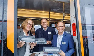 Das Foto zeigt drei Personen in der geöffneten Tür einer Tram-Train-Bahn. Abgebildet sind von links nach rechts Sonja Wiesholzer (Schiene Oberösterreich), Karsten Nagel (Saarbahn) und Christian Höglmeier (Albtal-Verkehrs-Geselllschaft/Verkehrsbetriebe Karlsruhe). Alle halten ein graues Fahrzeugmodell einer Bahn in der Hand. 