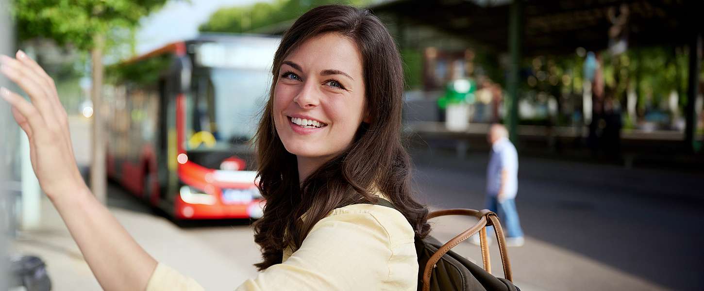 Une jeune femme se tient devant un distributeur de billets en souriant.