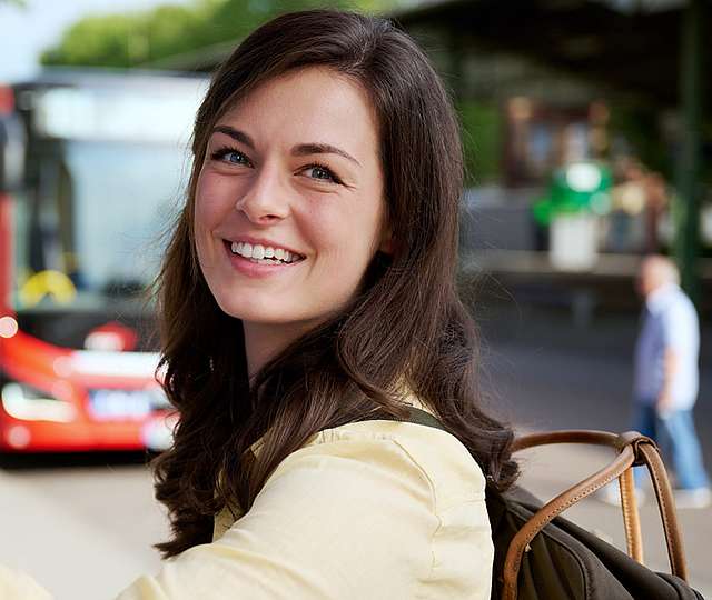 Une jeune femme se tient devant un distributeur de billets en souriant.